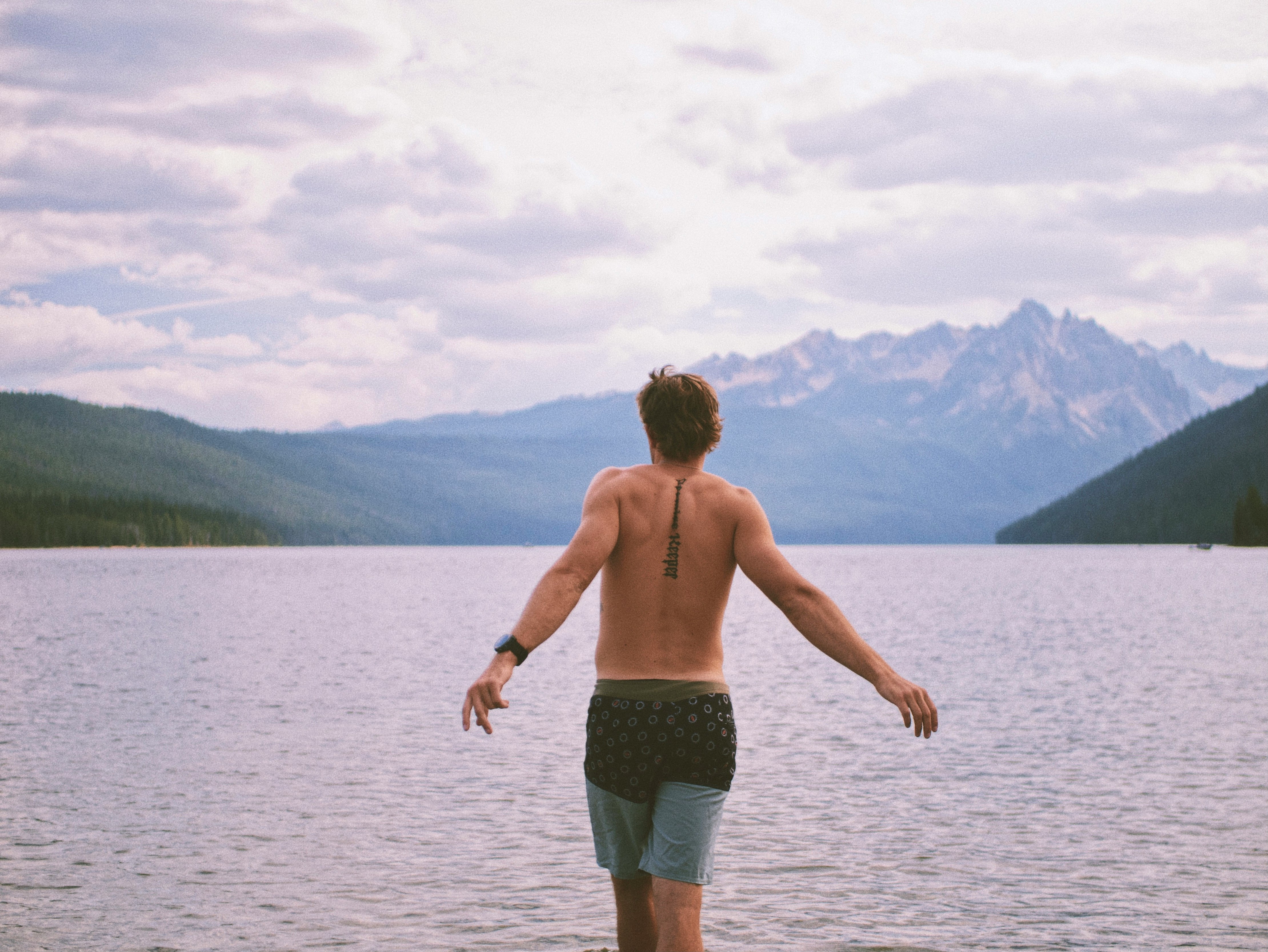 topless boy in black shorts standing on brown wooden dock during daytime